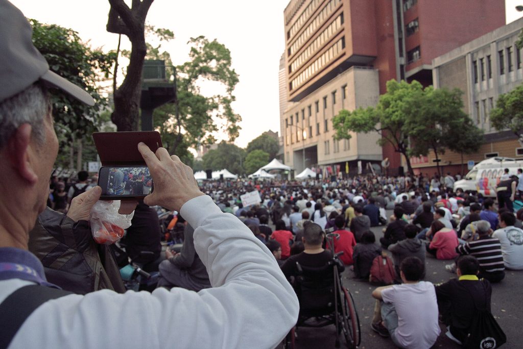 An elderly man uses his smartphone to video record the large crowd gathered on Jinan Road (濟南路)